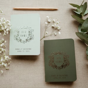 May include: Two small, green and light green vow books with silver foil lettering. The books are titled "Her Vows" and "His Vows" with the names Nikki & Salvatore and the date April 22, 2024.
