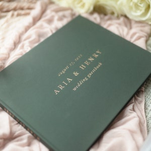 Może przedstawiać: Zielony, ślubny notes dla gości z pozłacanymi napisami. Tekst brzmi: "August 27, 2023, Aria & Henry, Wedding Guestbook".