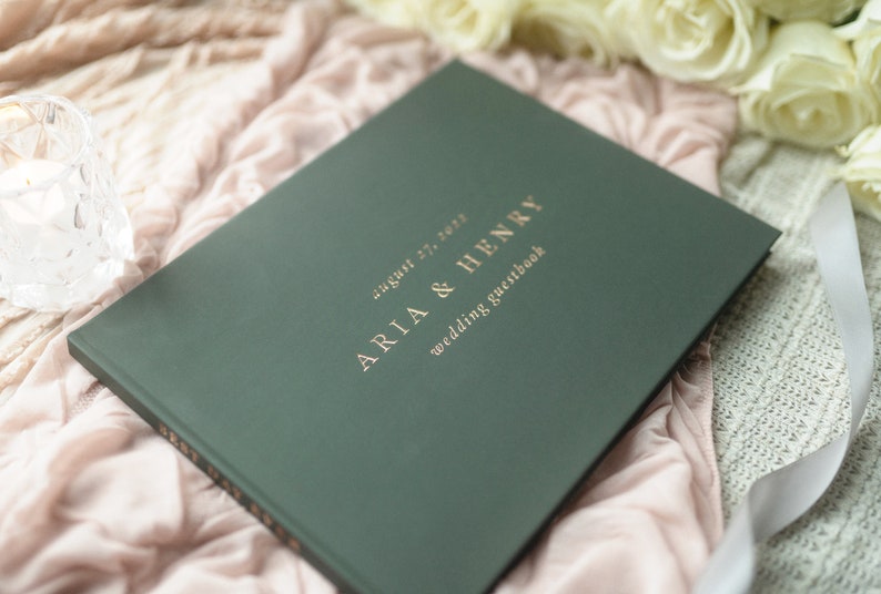 Może przedstawiać: Zielony, ślubny notes dla gości z pozłacanymi napisami. Tekst brzmi: "August 27, 2023, Aria & Henry, Wedding Guestbook".