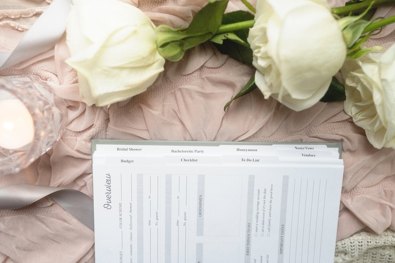 May include: A wedding planner with tabs labeled "Bridal Shower", "Bachelorette Party", "Honeymoon", and "Notes/Vows". The planner is open to the "Overview" page, which includes sections for "Color Scheme", "Budget", "Guests", and "First Things To Do".