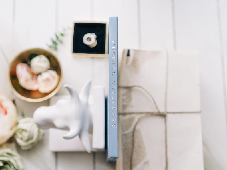 May include: A light blue book with the text "Wedding Guest Book" printed in silver on the spine.