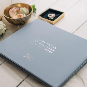May include: A light blue wedding guest book with the text "I have found the one whom my soul loves" printed in silver foil.