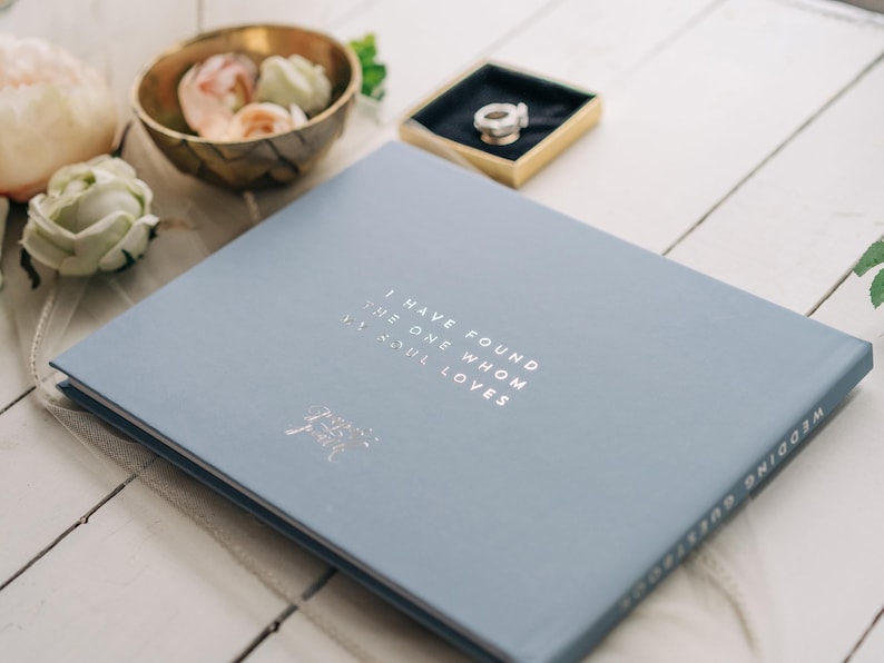 May include: A light blue wedding guest book with the text "I have found the one whom my soul loves" printed in silver foil.