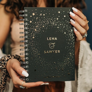 May include: A black wedding planner with gold glitter and stars. The cover reads "Lena & Sawyer" with a gold ampersand.