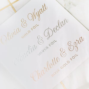 May include: White paper with gold, silver, and rose gold foil lettering. Names include Olivia & Wyatt, Amelia & Declan, and Charlotte & Ezra. The words "GOLD FOIL", "SILVER FOIL", and "ROSE GOLD FOIL" are also printed on the paper.