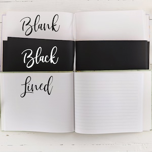 Może przedstawiać: Otwarty notes z trzema r&oacute;żnymi opcjami papieru: biały, czarny i w linie. Notes leży na białym drewnianym tle z kwiatami i zielenią.
