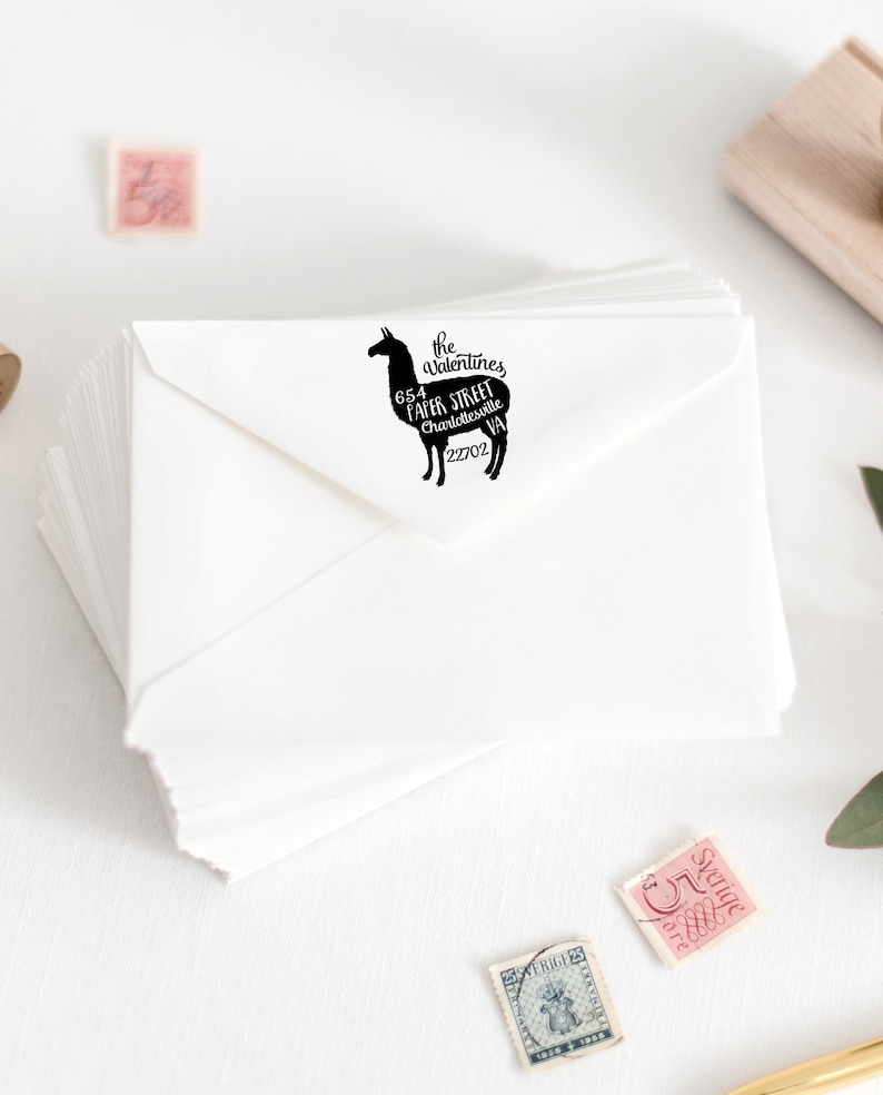 May include: A black and white rubber stamp featuring a llama silhouette with the text "The Valentines 654  Faircloth Street Charlottesville VA 22702" printed inside the llama.