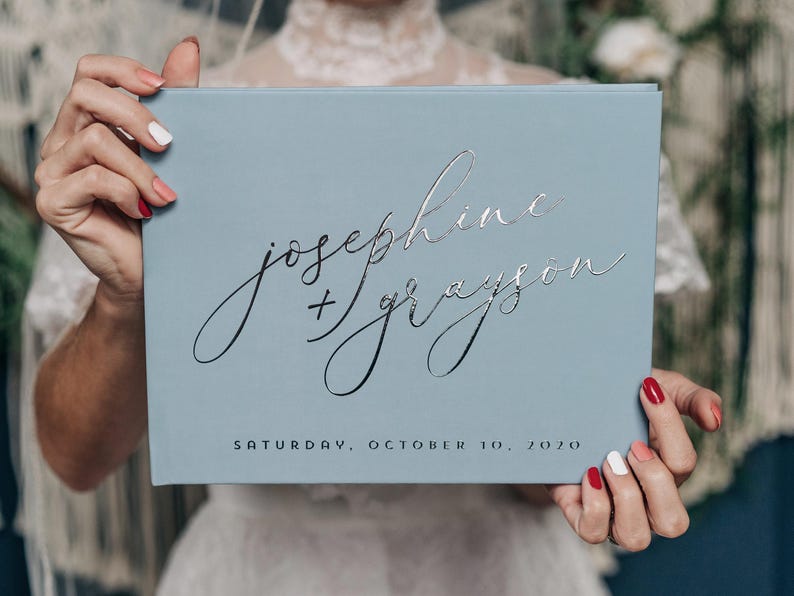 bride holding dusty blue elegant guestbook for guest to sign in on the book