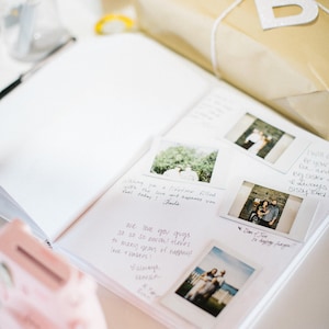 Może przedstawiać: Biały album ze zdjęciami z ręcznie napisanymi wiadomościami i zdjęciami Polaroid. Zdjęcia przedstawiają parę oraz ich przyjaci&oacute;ł i rodzinę. Album jest otwarty na stronie z wiadomością "We love you guys so so so much! There's to many years of happiness love + laughter!"