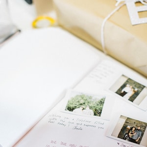 May include: A white notebook with handwritten messages and photos attached. The notebook is open and has a white background. The photos are of people and nature. The text in the notebook says "Bretone filled with the love and happiness you feel today! Charlie" and "we love you".