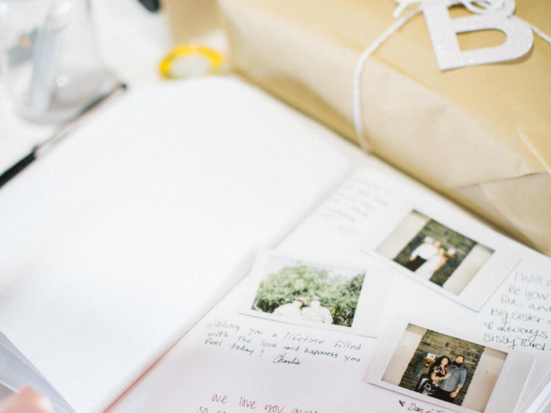 May include: A white notebook with handwritten messages and photos attached. The notebook is open and has a white background. The photos are of people and nature. The text in the notebook says "Bretone filled with the love and happiness you feel today! Charlie" and "we love you".