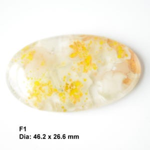 May include: A white oval cabochon with yellow and orange inclusions. The stone measures 46.2 mm by 26.6 mm. F1.