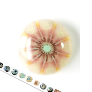 Puede incluir: Una cuenta de vidrio redonda con un diseño de flor rosa y blanca. La flor tiene un centro verde claro y acentos amarillos.