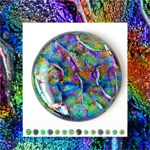 May include: A dichroic glass cabochon with a round shape. The glass displays a vibrant array of colors, including blues, greens, purples, and golds, creating an iridescent effect. The cabochon is likely used for jewelry making or other decorative purposes.