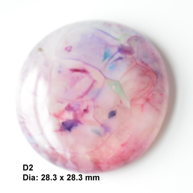 May include: A round, translucent, pink, purple, and blue resin cabochon with a marbled pattern.  The cabochon is approximately 28.3 mm in diameter.  D2.
