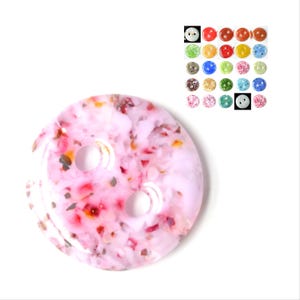 Può includere: Un bottone rosa a due fori con un motivo maculato di bianco, rosso e giallo. Il bottone è in plastica e ha una finitura lucida.