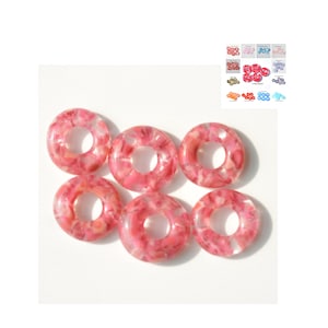 Puede incluir: Seis cuentas rosadas en forma de donut con un patrón de mármol. Las cuentas son de vidrio y tienen un acabado transparente y claro.