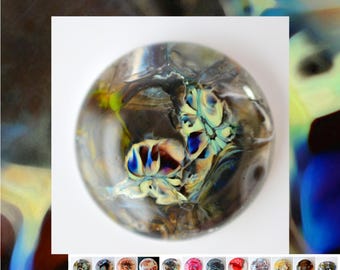 May include: A round, glass paperweight with an abstract design. The paperweight features swirls of blue, yellow, brown, and white colors. The design is encased in clear glass, creating a unique decorative item.