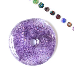 May include: A purple glass bead with a hole in the center. The bead is covered in iridescent glitter.
