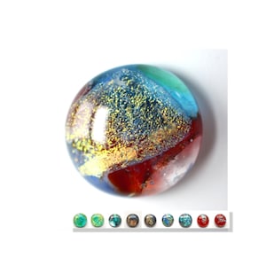 Puede incluir: Un cabujón redondo de vidrio multicolor con motas doradas. El cabujón tiene tonos de azul, verde, rojo y blanco.