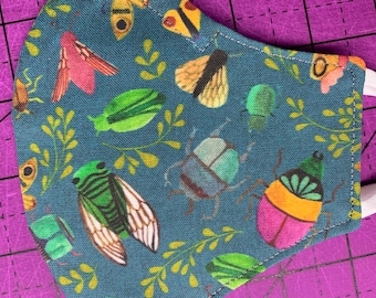 May include: A blue fabric face mask with a repeating pattern of green, pink, and yellow insects and leaves.