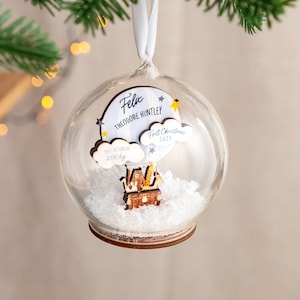 May include: A glass ornament with a wooden hot air balloon inside. The balloon has a cloud with the text "Felix Theodore Huntley, 21st October 3.570 kg, First Christmas 2023".