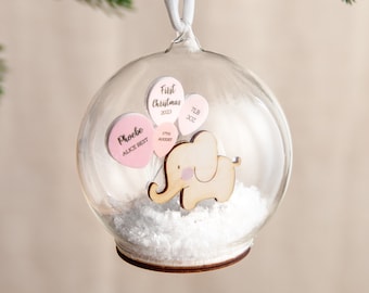 May include: A clear glass ornament with a wooden elephant holding pink balloons. The balloons have the text "First Christmas 2023", "Phoebe Alice Best", "17th August", and "7lb 3oz".