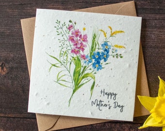Peut inclure: Une carte blanche avec une illustration aquarelle d'un bouquet de fleurs roses et bleues. La carte porte le texte "Happy Mother's Day" imprimé dessus.