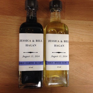 May include: Two glass bottles with labels. The bottles are labeled "Jessica & Bill Hagan" and the date "August 15, 2014". One bottle is filled with a dark liquid and labeled "Garlic Cilantro Balsamic" and the other bottle is filled with a light liquid and labeled "Garlic Infused Olive Oil". Both bottles are 60 ml.