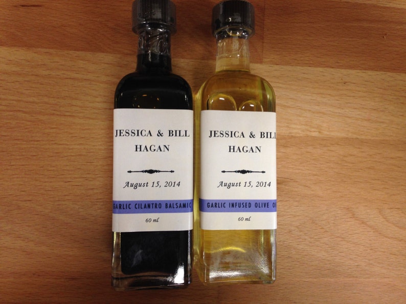 May include: Two glass bottles with labels. The bottles are labeled "Jessica & Bill Hagan" and the date "August 15, 2014". One bottle is filled with a dark liquid and labeled "Garlic Cilantro Balsamic" and the other bottle is filled with a light liquid and labeled "Garlic Infused Olive Oil". Both bottles are 60 ml.
