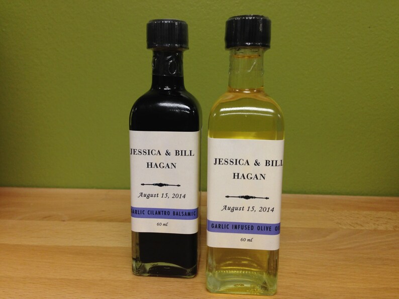 May include: Two glass bottles with labels. The bottles are labeled "Jessica & Bill Hagan" and the date "August 15, 2014". One bottle is labeled "Garlic Cilantro Balsamic" and the other is labeled "Garlic Infused Olive Oil". Both bottles are 60 ml.