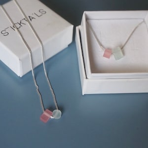 Può includere: Due collane d'argento con catene delicate e piccole perle di pietre preziose colorate. Le collane sono esposte in scatole bianche con il nome del marchio "STICKTALS" stampato su una delle scatole.