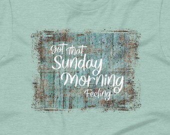 May include: A light blue t-shirt with a distressed, teal and brown background. The text "Got that Sunday Morning Feeling" is written in white on the background.