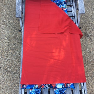 May include: A red sleeping bag with a Spiderman themed pillow and blanket. The sleeping bag is folded and placed on a wooden bench.