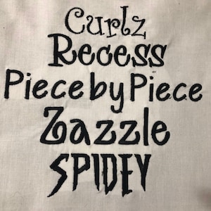 May include: A white fabric surface with black embroidered text that reads "Curlz Recess Piece by Piece Zazzle SPIDEY".