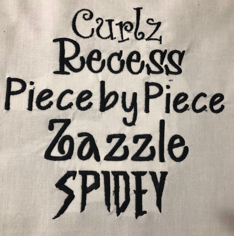 May include: A white fabric surface with black embroidered text that reads "Curlz Recess Piece by Piece Zazzle SPIDEY".