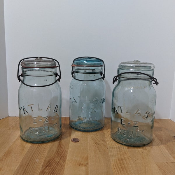 Three Atlas E-Z Seals bale jars with glass lids. One is deep aqua blue and two are a watery, pale greenish blue. Lots of bubbles & style.