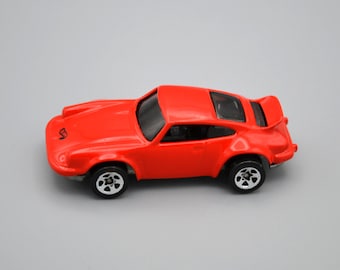 May include: A red toy car with a black spoiler and black wheels. The car has a clear windshield and a black interior.