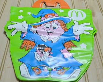 May include: A green Halloween-themed McDonald's Happy Meal bag featuring a cartoon witch with orange hair and a blue dress. The bag has a handle and the McDonald's logo.