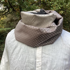 Könnte beinhalten: Ein brauner und cremefarbener Infinity-Schal mit einem kleinen Blumenmuster. Der Schal ist aus einem weichen, seidenartigen Stoff.