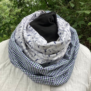 Könnte beinhalten: Ein reversibler Schal mit weißem Hintergrund und einem blau-grünen Karomuster auf der einen Seite und einem weißen Hintergrund mit einem blauen Blumenmuster und Hirschsilhouetten auf der anderen Seite.