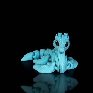 Peut inclure: Un jouet de dragon articul&eacute; bleu clair avec des yeux noirs. Le dragon est en position assise, la t&ecirc;te l&eacute;g&egrave;rement inclin&eacute;e sur le c&ocirc;t&eacute;.
