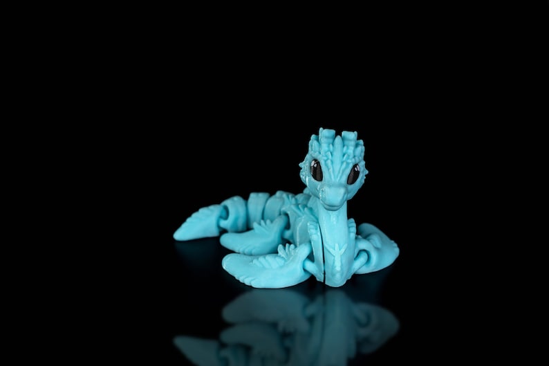 Peut inclure: Un jouet de dragon articul&eacute; bleu clair avec des yeux noirs. Le dragon est en position assise, la t&ecirc;te l&eacute;g&egrave;rement inclin&eacute;e sur le c&ocirc;t&eacute;.
