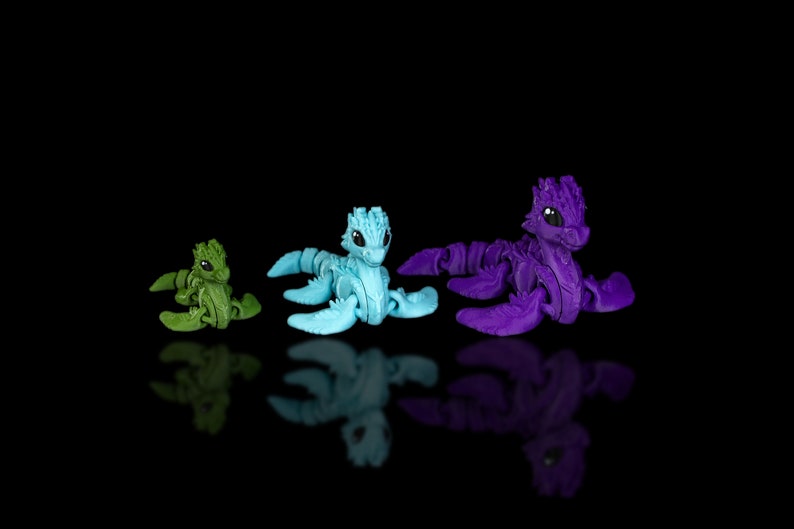 Peut inclure: Trois petites figurines de dragon articul&eacute;es en plastique de diff&eacute;rentes couleurs. Le dragon &agrave; gauche est vert, le dragon du milieu est bleu et le dragon &agrave; droite est violet.