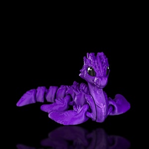 Peut inclure: Un jouet de dragon articul&eacute; violet avec des yeux noirs. Le dragon est en position de nage avec ses ailes d&eacute;ploy&eacute;es.