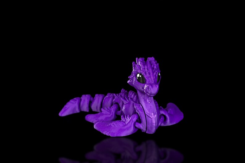 Peut inclure: Un jouet de dragon articul&eacute; violet avec des yeux noirs. Le dragon est en position de nage avec ses ailes d&eacute;ploy&eacute;es.