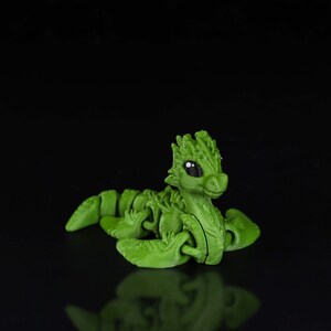 Peut inclure: Un jouet de dragon articul&eacute; vert avec de grands yeux et un corps segment&eacute;. Le dragon est en position recourb&eacute;e, la t&ecirc;te lev&eacute;e.