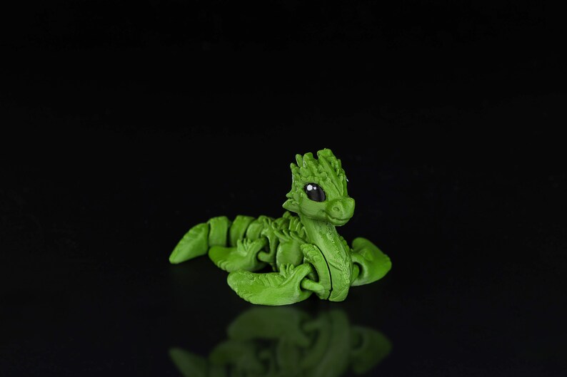 Peut inclure: Un jouet de dragon articul&eacute; vert avec de grands yeux et un corps segment&eacute;. Le dragon est en position recourb&eacute;e, la t&ecirc;te lev&eacute;e.