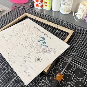 Preparing a personalized 11x14 USA push pin travel map for framing at JW Design Studio Gifts. The map is printed in-house on 100% cotton canvas and designed to be customized with watercolor paints, making it a unique travel keepsake for couples and adventure lovers.