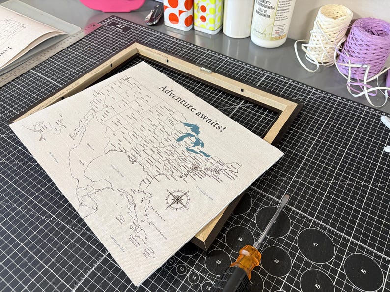 Preparing a personalized 11x14 USA push pin travel map for framing at JW Design Studio Gifts. The map is printed in-house on 100% cotton canvas and designed to be customized with watercolor paints, making it a unique travel keepsake for couples and adventure lovers.